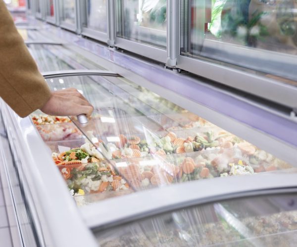 A man in a beige coat in the frozen food section of a large supe